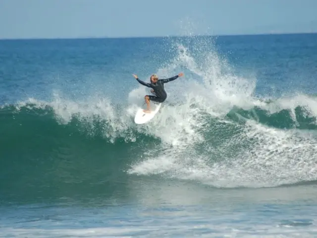 In the center of the image we can see a man is surfing on the wave. In the background of the image...