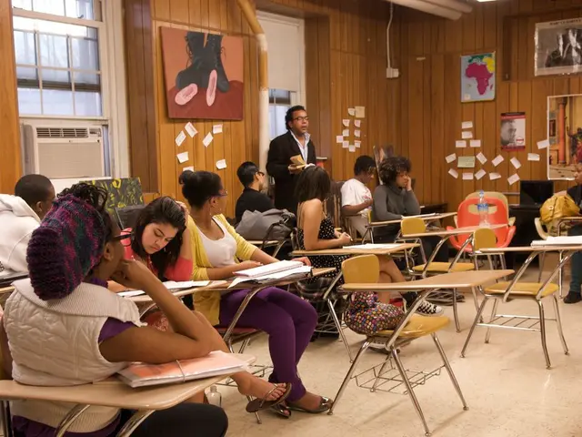 There are many people sitting in a class room in their chairs and one guy is standing and teaching...